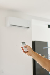 Close-up of hand using remote control to adjust temperature on wall-mounted air conditioner....