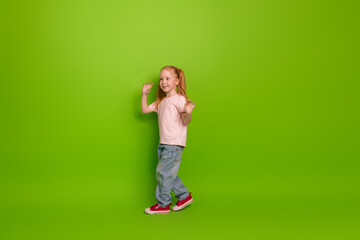 Adorable young girl posing on a vibrant green background showing a playful gesture wearing casual...