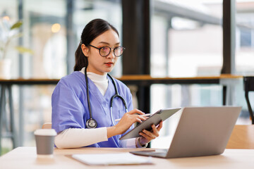 Female medical intern in blue medical scrubs e-learning on laptop computer at the ordination,...