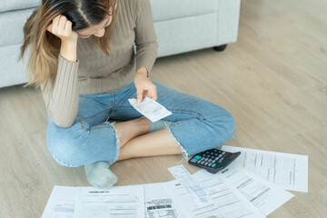 Stressed and headache asian woman with large bills or invoices no money to pay to expenses and...