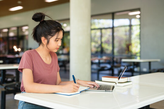 Focused asian teen girl student writing notes in notebook distance learning studying online makes goals check list at cafeteria. college school education, elearning concept.