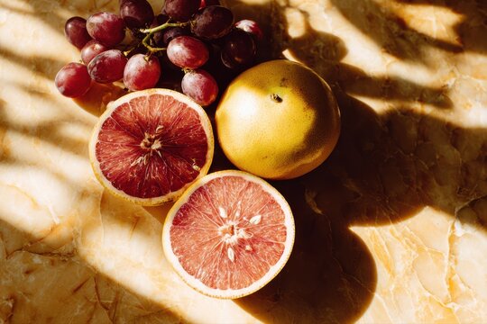A variety of colorful fruits, including a bunch of grapes and a single grape, arranged on a table in a flat lay style with shadows.