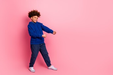 Joyful young boy gesturing playfully in casual blue hoodie against a vibrant pink background,...