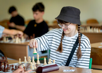A young woman in glasses concentrates on a move while playing chess. A girl plays in a chess tournament.  Girl at the chessboard. Tournament, portrait of teenage girl playing chess	