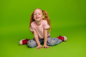 Smiling young girl with red hair sitting on a green backdrop in casual wear symbolizing joy and...