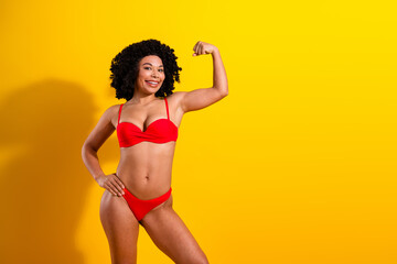 Confident woman in red swimsuit posing against a vibrant yellow background, emphasizing strength,...