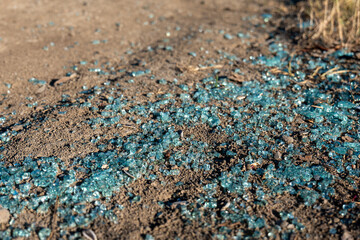 Broken car window glass on the ground. Blue-green safety glass shards scattered on dry soil. Sign of car break-in, accident or vandalism.