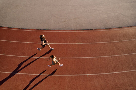 Two athletes running on track from above with long shadows - Powered by Adobe