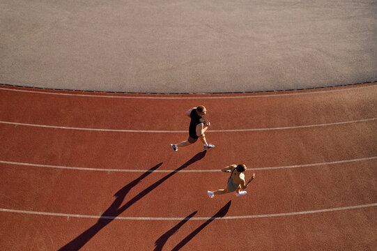 Two athletes running on track from above with long shadows - Powered by Adobe