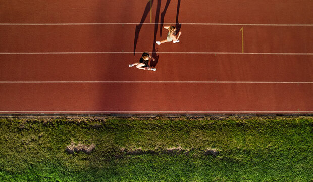 Aerial view of couple jogging on running track with long shadows - Powered by Adobe