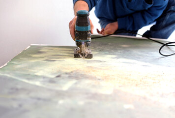 Nahaufnahme einer Stichsäge in Betrieb in der Hand eines Handwerkers im Hintergrund, der kniend...