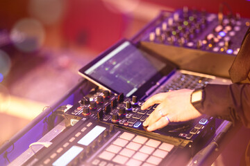 Close-up of a DJ mixing music with professional audio equipment during a live event. Warm lights...