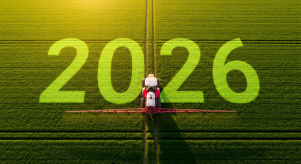 Aerial View of Tractor Spraying Crops in a Field with 2026 Written on the Ground