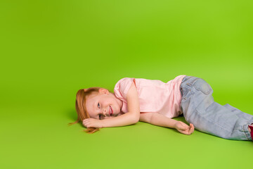 Young girl with red hair smiling while lying on the green background in a casual outfit expressing happiness and joy