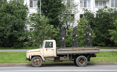 An old, rusty truck with an open back is parked near a lawn, Tovarischesky Prospekt, Saint Petersburg, Russia, July 09, 2025