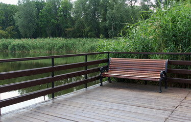 A wooden bench on a deck overlooking a calm river surrounded by lush green vegetation. The scene is tranquil and inviting