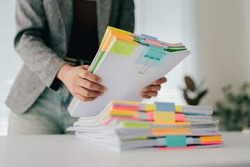 Young female employee is working with a pile of documents to search for information and check documents on the table. Document search concept.