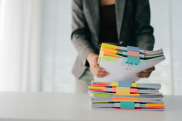 Young female employee is working with a pile of documents to search for information and check...
