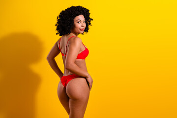 Confident young woman in red lingerie posing against a vibrant yellow background showcasing beauty and self-assurance.