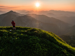 Aerial view of man on top of a mountain at sunset with mountain range in the background. Achenkirch, Tirol, Austria