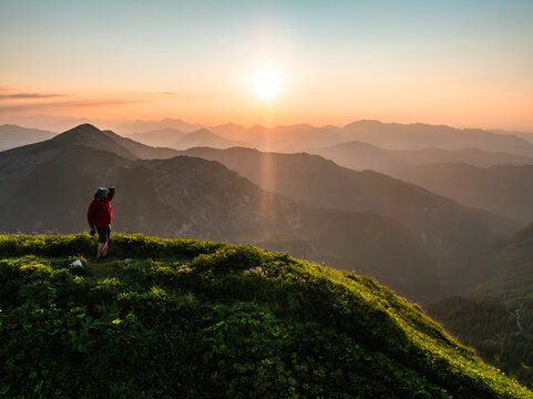 Aerial view of man on top of a mountain at sunset with mountain range in the background. Achenkirch, Tirol, Austria