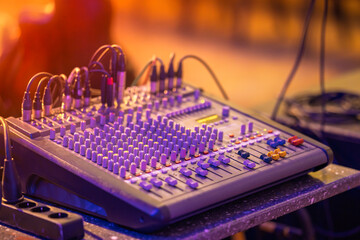 Professional audio mixing console with colorful knobs and faders, captured under stage lighting....