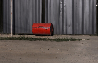 a trash can from an old red barrel on the background of a gray metal fence