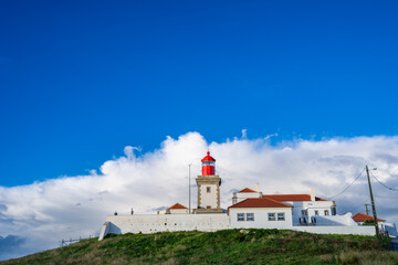 Iconic Cabo da Roca lighthouse on the westernmost point of mainland Europe in Portugal, set against a dramatic blue sky with white clouds.