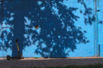 a blue wall of a building with a shadow from a tree and an electric scooter nearby