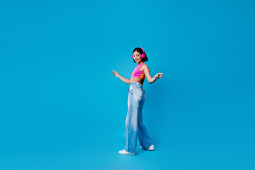Young woman dancing with headphones on a vibrant turquoise background enjoying a lively mood and...