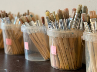 Various paintbrushes organized in clear jars on a table ready for use in an art studio setting.