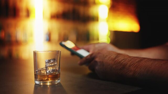 Man scrolling media on cellphone while drinking whiskey in bar, feeling isolated