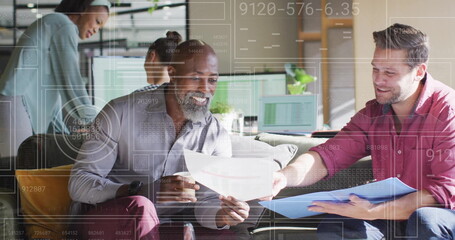 Reviewing colleagues exchanging printed reports and discussing data in office lounge, with charts