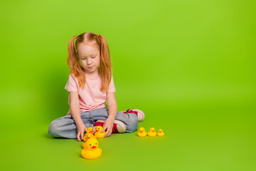 Cute girl arranging painted rubber ducks sitting on a vibrant green background in casual clothing