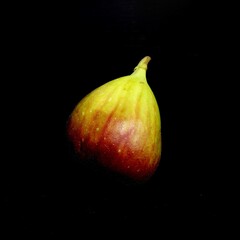 Artistic photograph featuring a fig set against a dark background. The vibrant red flesh are...