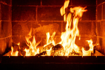Bright fireplace flame consuming wooden logs, rustic warmth, glowing ambiance, interior brick wall, cozy home feeling, winter evening heat, traditional heating symbol, peaceful indoor mood