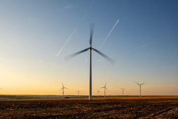 Wind turbines standing tall in agricultural plain, working silently to generate electricity from air currents, renewable source usage, solar-lit background, ecological power plant landscape photo.