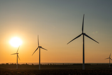 Wind power station across farmland during calm evening, spinning turbine blades generating clean electricity, renewable infrastructure, natural resource usage, sustainable environmental electricity