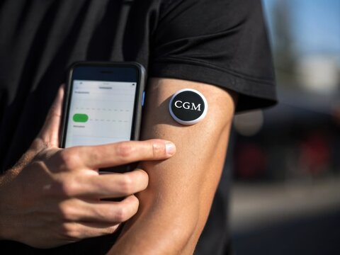 A person checks a continuous glucose monitor on their arm using a smartphone.