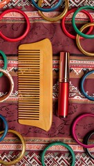 Still life featuring a wooden comb, red lipstick, and vibrant bangles arranged on a richly patterned textile background.
