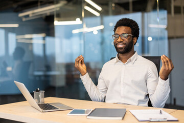 An African-American man practices meditation at his office desk, promoting mindfulness and...