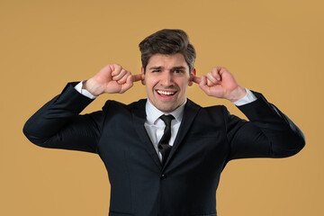 Businessman covering ears, showing irritation in beige studio. Stress, overload