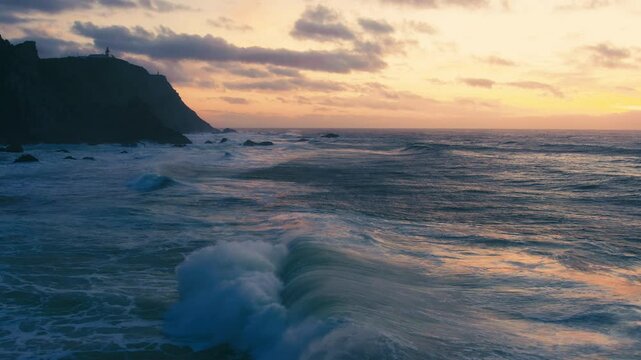 The stunning coastal view at sunset is mesmerizing as waves crash against majestic cliffs, and the colorful sky transforms, creating a beautiful scene of natural beauty, peace, and relaxation