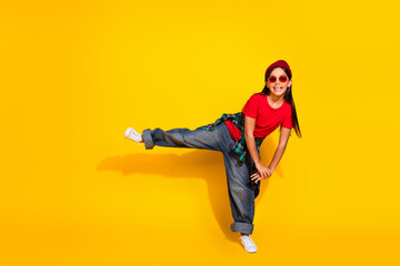 Cheerful young girl in casual style clothing posing in a fun stance against a vibrant yellow...