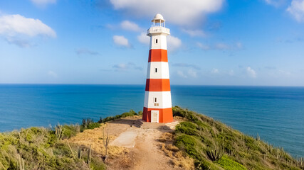 Red and white lighthouse is on a rocky cliff overlooking the ocean