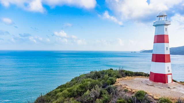 Red and white lighthouse is on a rocky cliff overlooking the ocean - Powered by Adobe