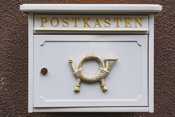 White mailbox with historic post horn relief hanging on a brown wall outside
