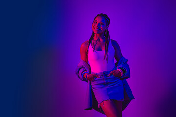 Fototapeta premium Confident young woman posing in vibrant neon lighting wearing casual denim and expressing charm and joy