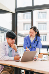 Two healthcare professionals, one male and one female, discussing patient information at desk with laptop in bright modern office, teamwork and collaboration