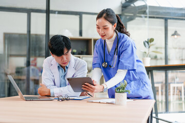 Two healthcare professionals, one male and one female, collaborate in modern office setting, reviewing patient information on digital tablet, displaying teamwork and focus